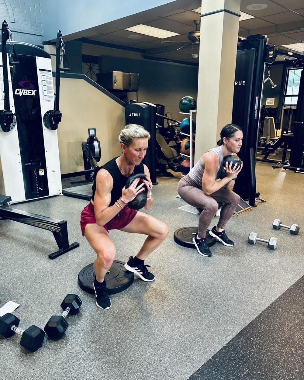 Sara and Meredith squatting with medicine balls during a community strength session