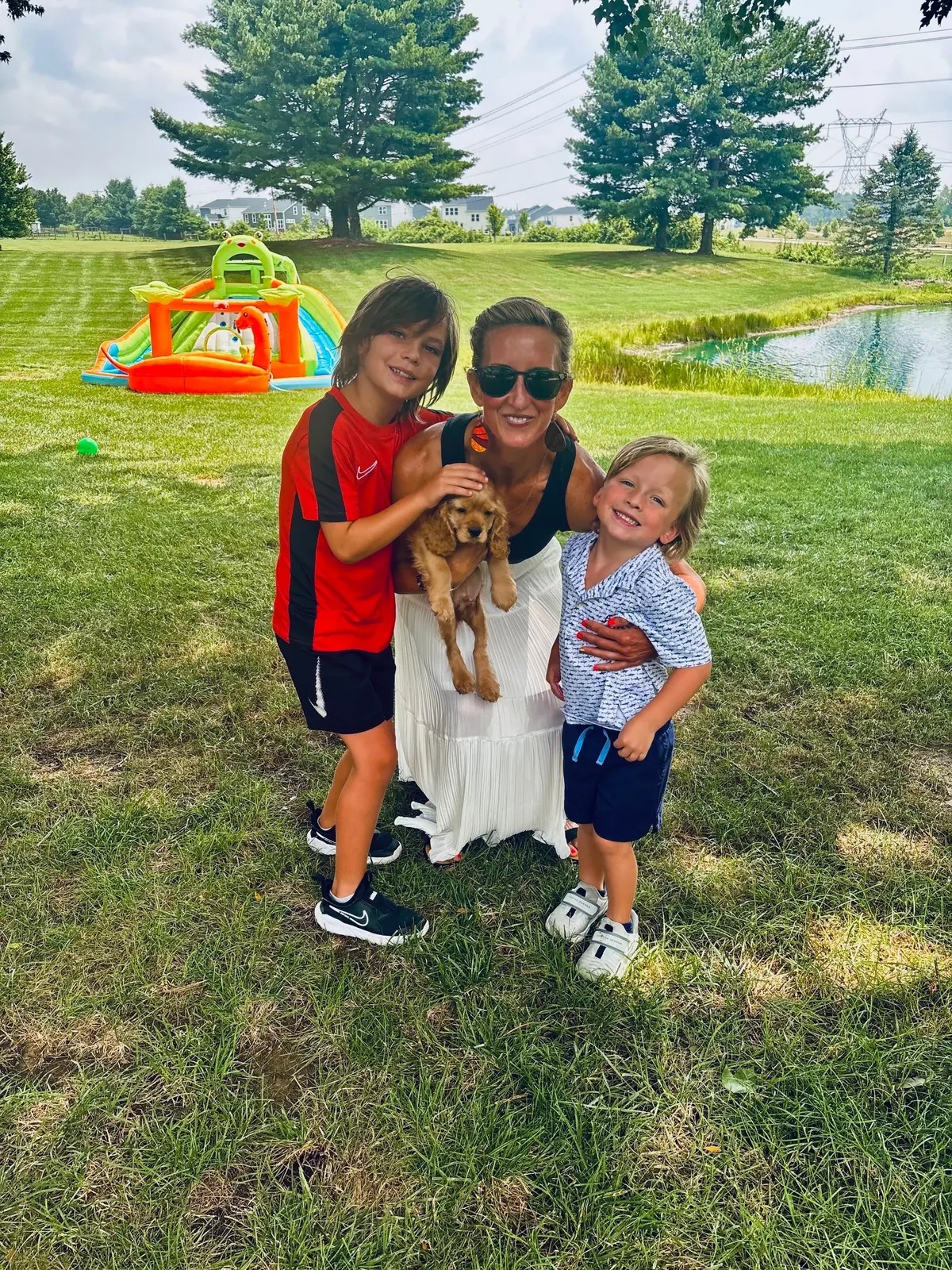Meredith with Mak, Crew, and a puppy outdoors by the pond